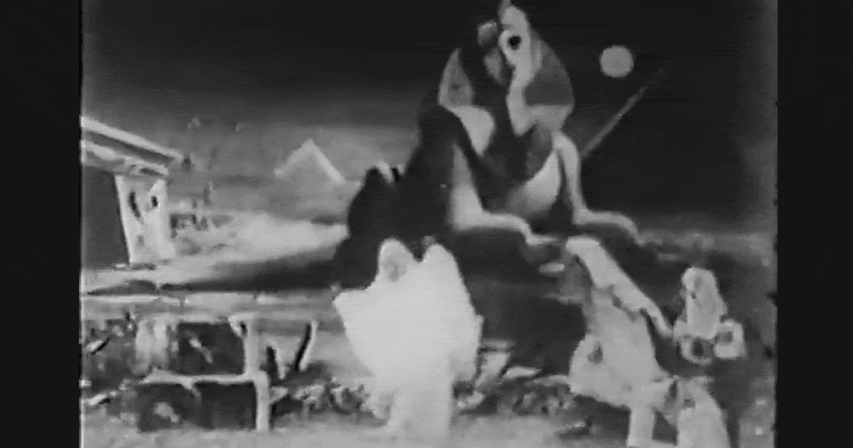 Black and white video clip of three dancing figures in white, flowing robes in front of an Egyptian sphynx.